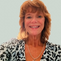 Woman with shoulder-length reddish hair, wearing a leopard print top and a rose pendant necklace, smiling.