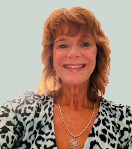 Woman with shoulder-length reddish hair, wearing a leopard print top and a rose pendant necklace, smiling.